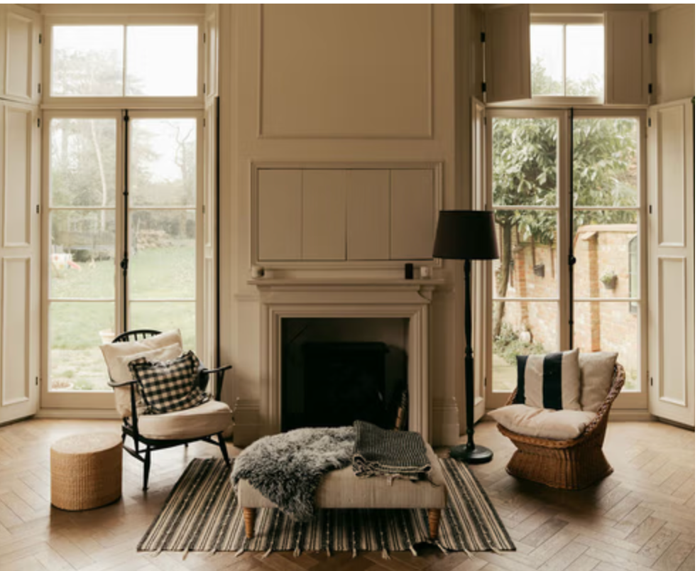 Bright living room at Walton House with fireplace, French windows, parquet floor and neutral interiors overlooking the garden.