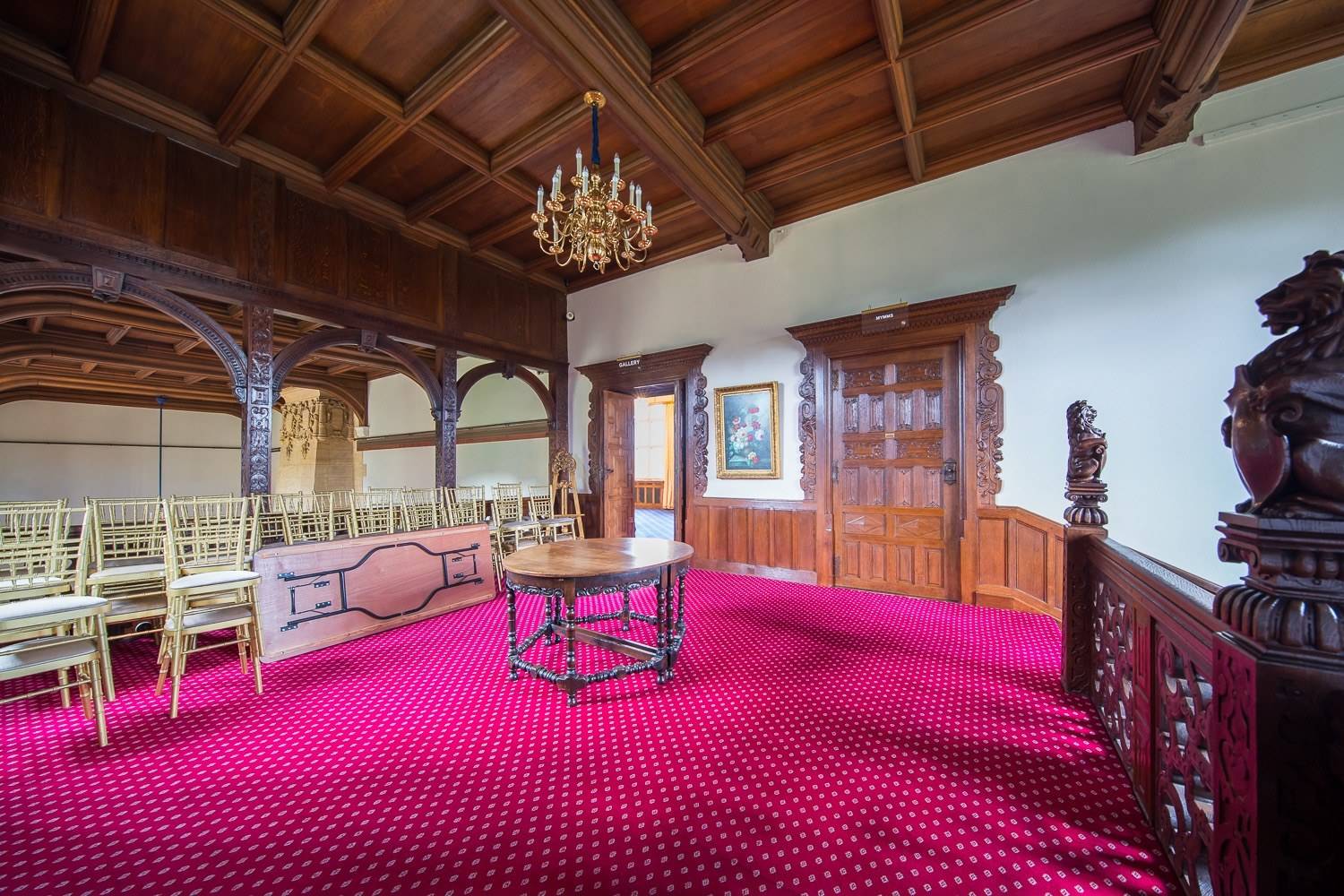 Elegant period anteroom with exposed oak framework, brass chandelier, and vibrant red carpeting via Love Locations.