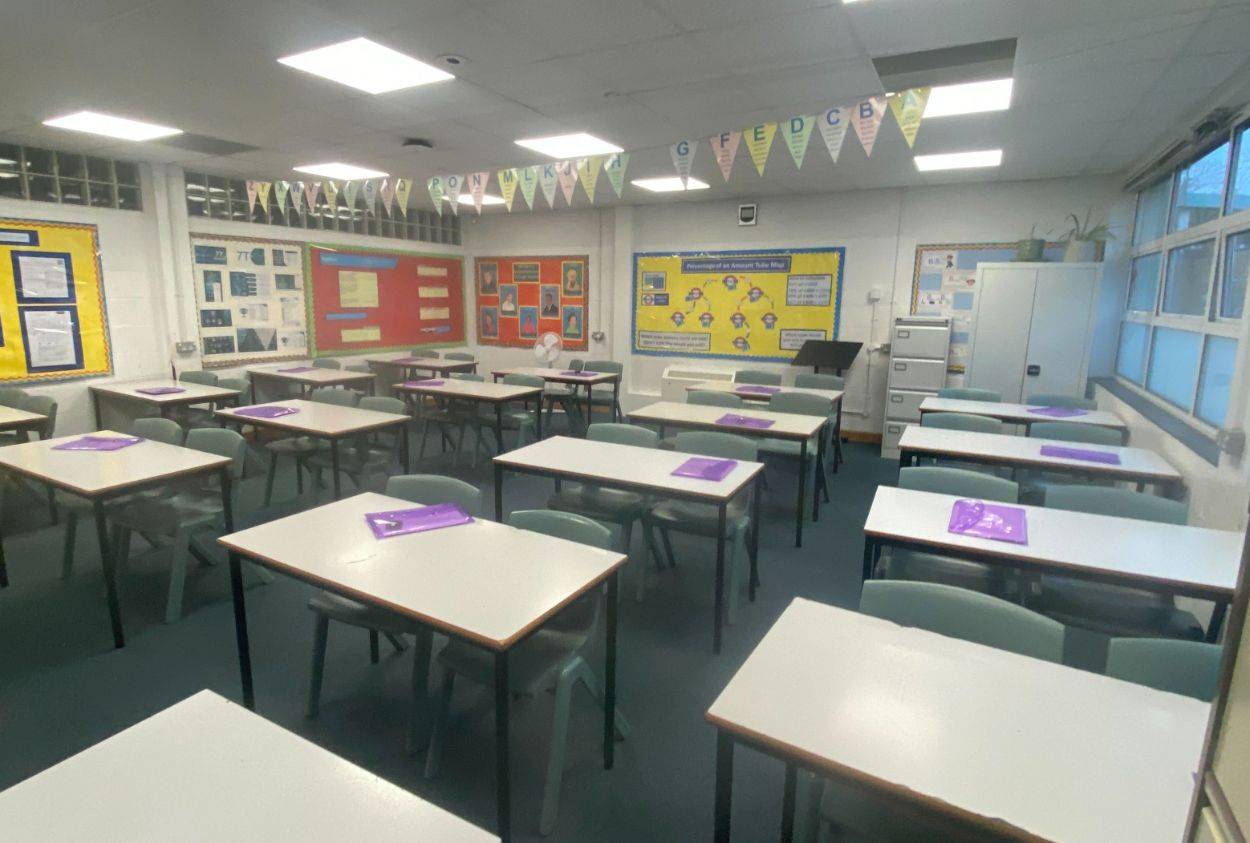 Organized secondary school classroom shoot space with grey student desks, wall displays, and ceiling lighting via Love Locations.