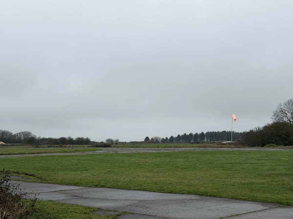 Vast open grass airfield runway stretching toward tree lines under an overcast sky in Corby, NN17, managed by Love Locations.