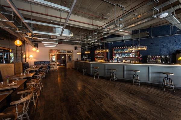 Spacious industrial-chic restaurant shoot location on Streatham Hill, South West London SW16 featuring polished dark wood floors and an expansive curved zinc bar counter, ideal for commercial brand filming via Love Locations.