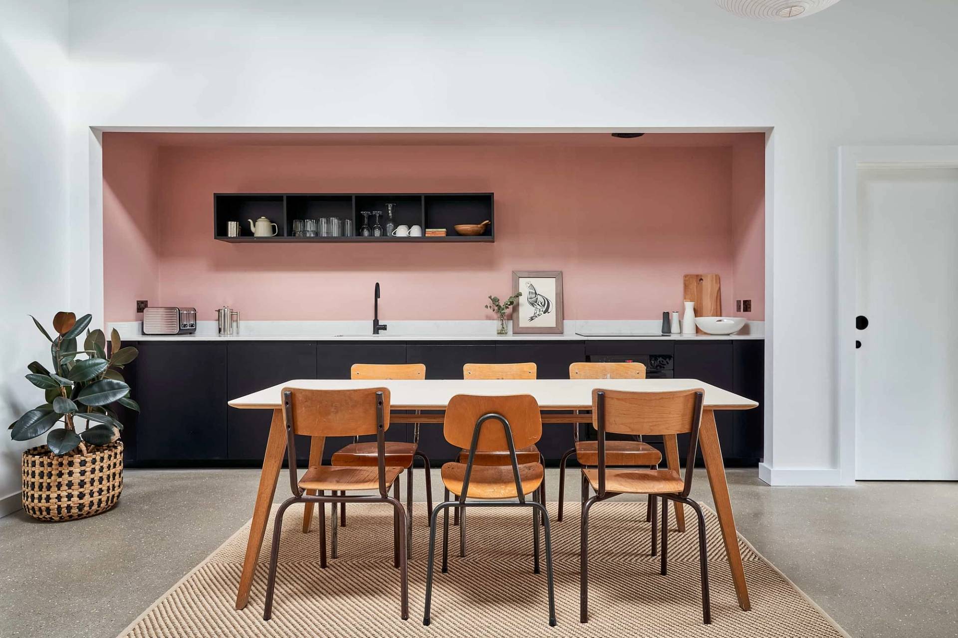 Terracotta pink dining nook featuring a white dining table, wooden chairs, and dark wall shelving, Love Locations IP30.