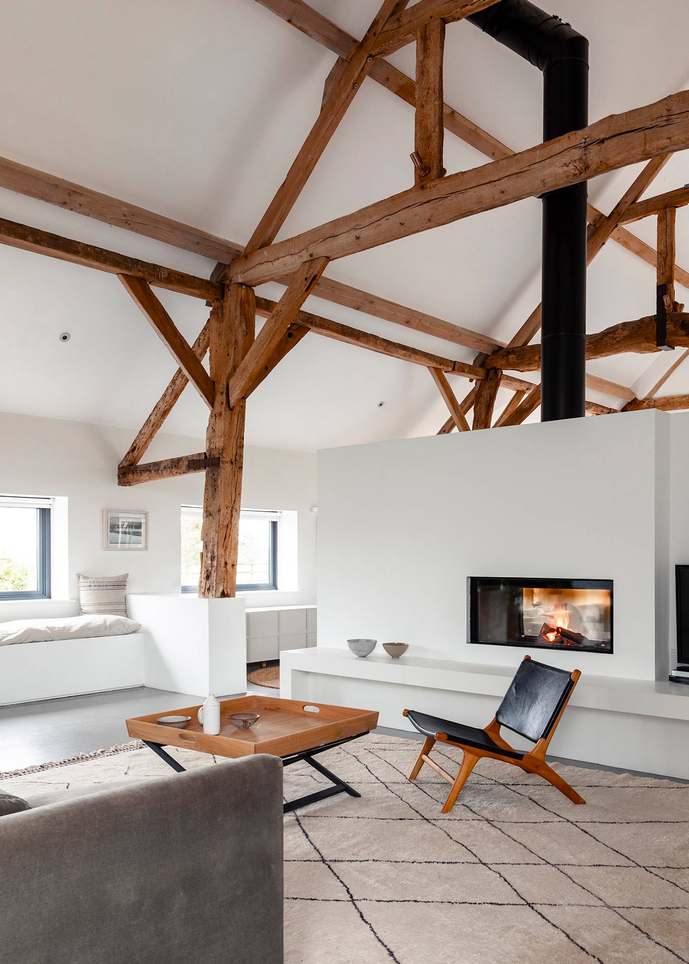 Cozy fireplace nook with a mid-century leather armchair set under exposed timber trusses, Love Locations SN8.