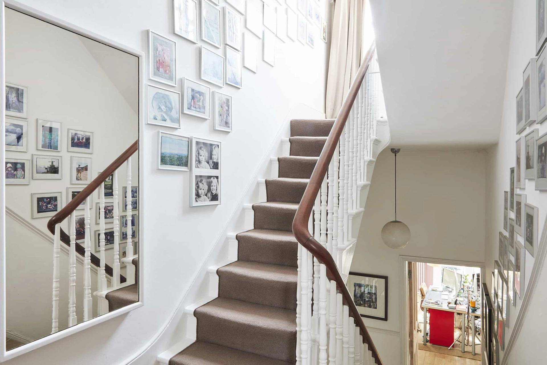 Classic staircase transition with white spindles, brown carpet runner, and gallery wall art frames, Love Locations N5.