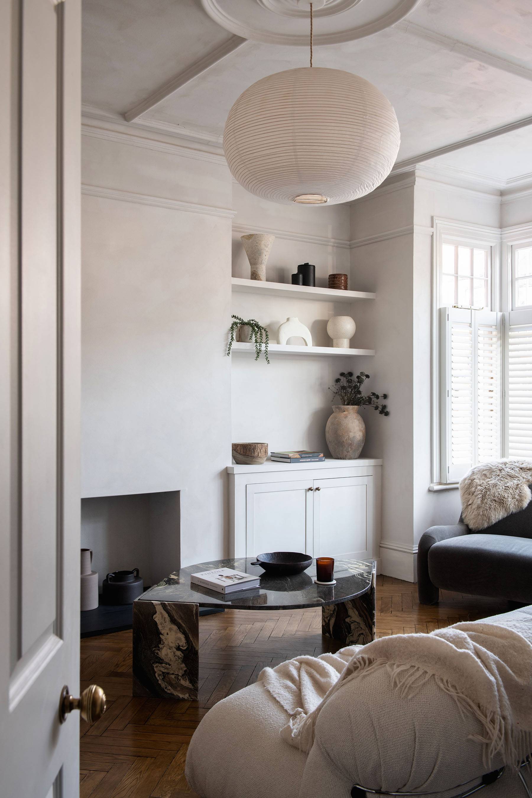 Light-filled living room featuring textured plaster walls, bay windows with white shutters, and neutral curved sofa, Love Locations SW16.