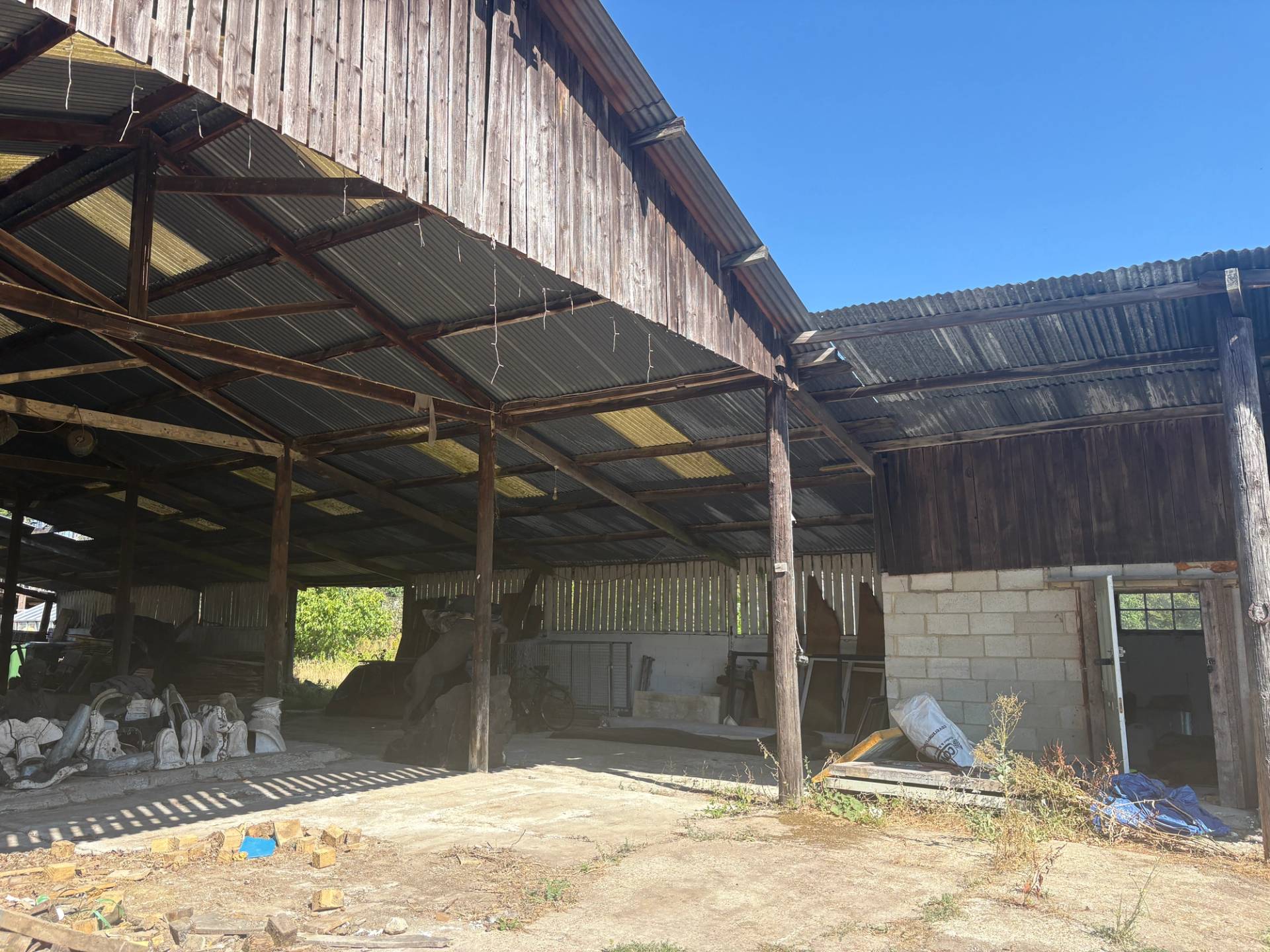 Open-sided timber pole barn with corrugated metal roof panels and concrete yard floor on an industrial farm location in South Chailey, Love Locations BN8.