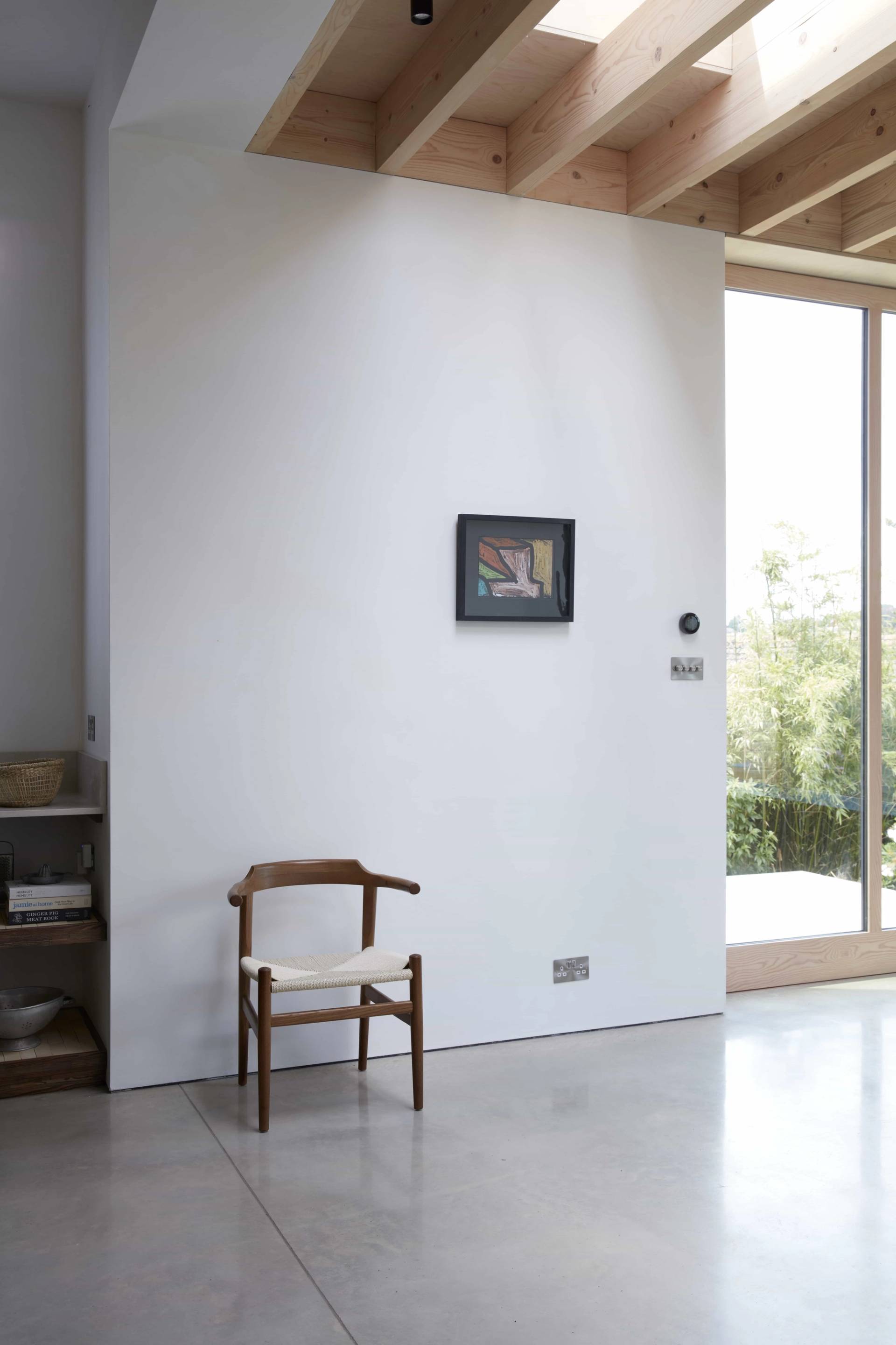 Minimalist plaster wall hallway transition with a single wooden armchair and glass door garden views, Love Locations TN34.