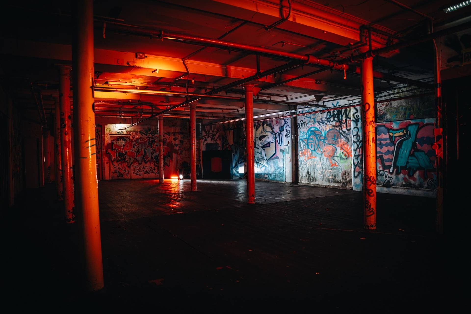 Sprawling underground warehouse shoot space in a Cheetham Hill venue in Manchester M3 from Love Locations, featuring graffiti-covered walls, industrial cast-iron pillars, and red and orange ambient strip lighting.