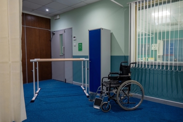 Rehabilitation room with parallel support bars, wheelchair, and blue wall panelling, Love Locations UB4.