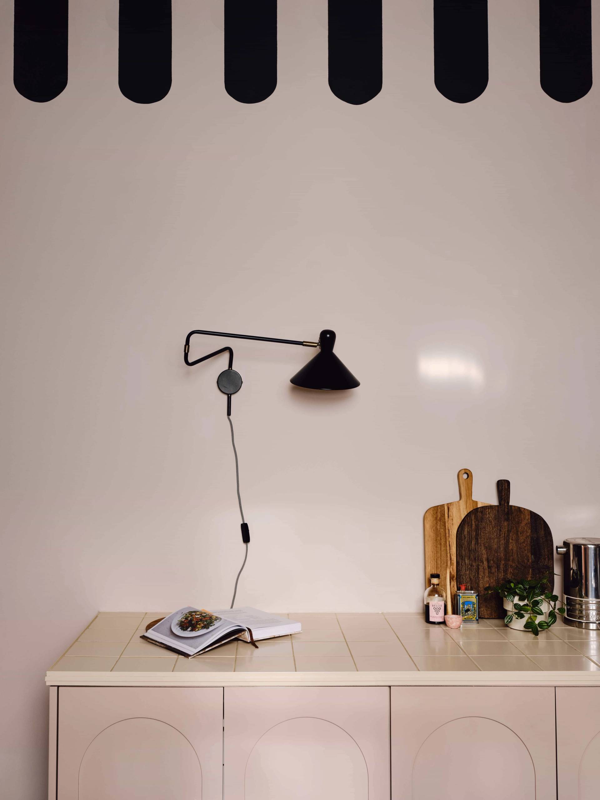 Pink kitchen counter workspace styled with a black swing-arm wall light and wooden cutting boards, Love Locations CR0.