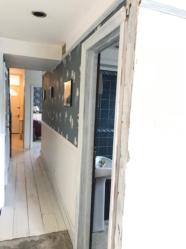 Narrow residential corridor leading past a vintage dark blue tiled bathroom doorway, suitable for gritty crime drama scene scouting, Love Locations.