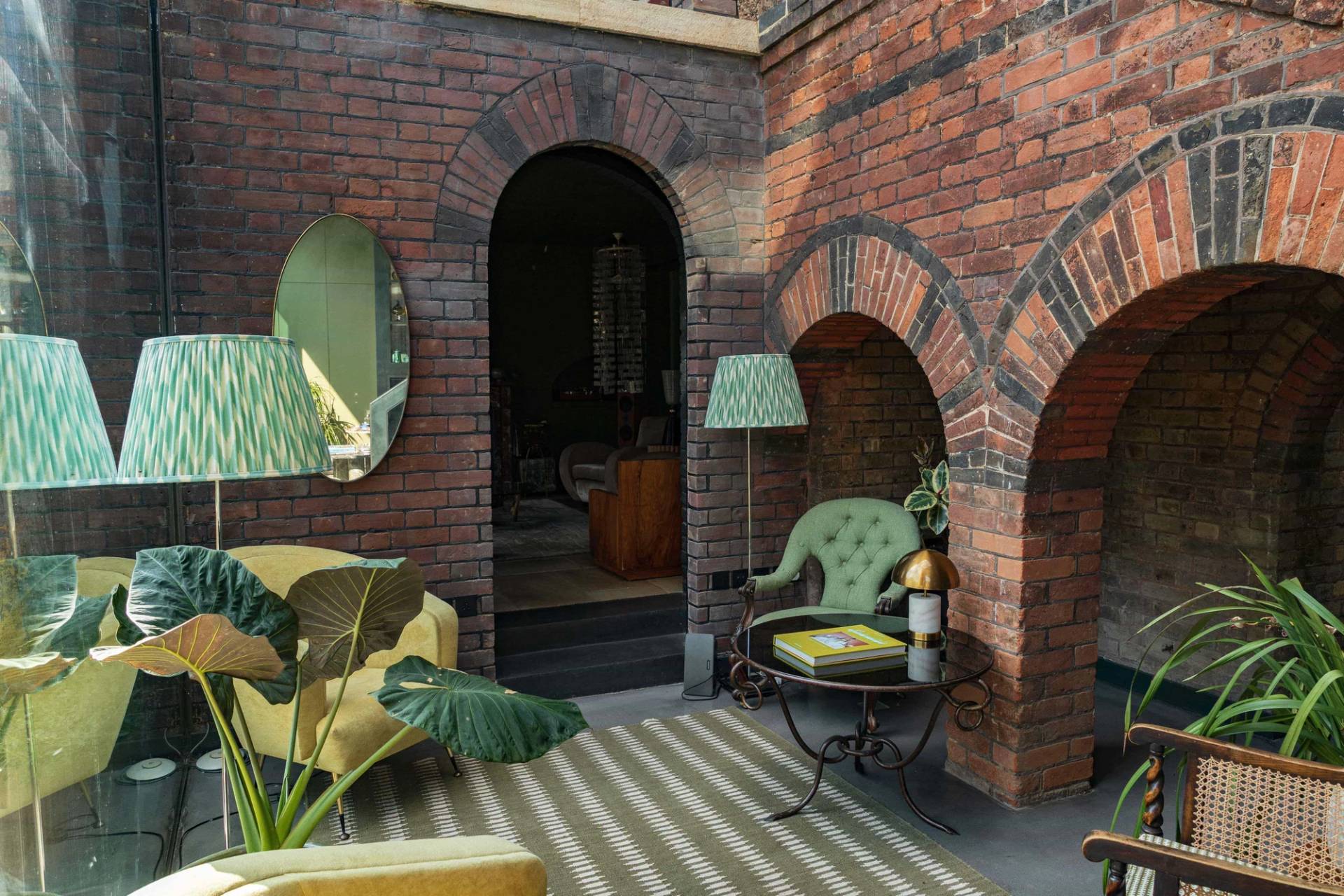 Elegantly styled brick archway seating area with a striped rug, green armchair, and vintage floor lamp, Love Locations SW20.