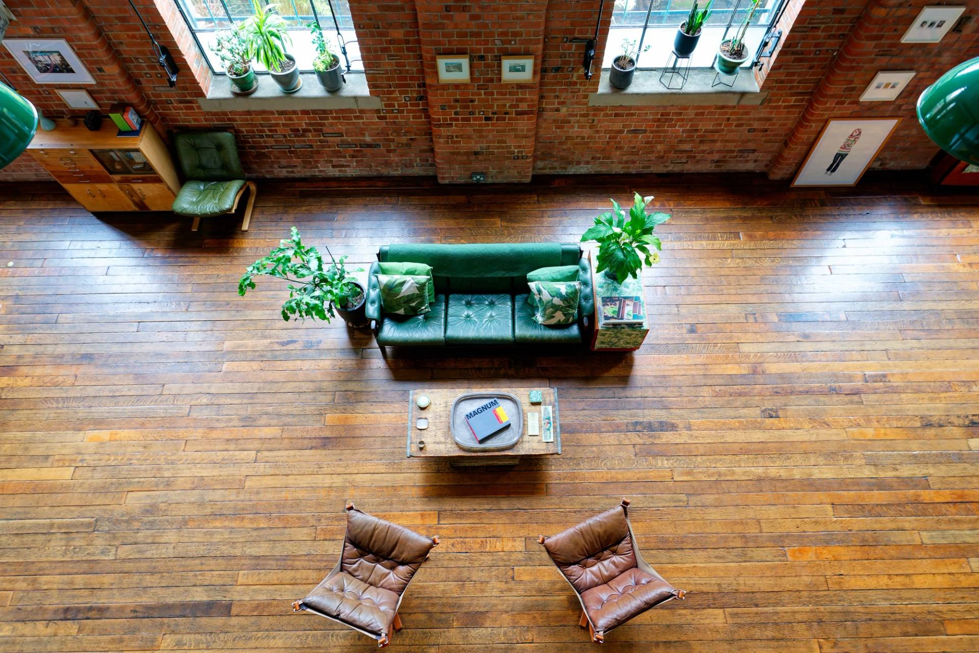 High-angle shot of a green sofa setup, timber coffee table, and leather armchairs on dark wood floors in a warehouse loft, Love Locations E14.