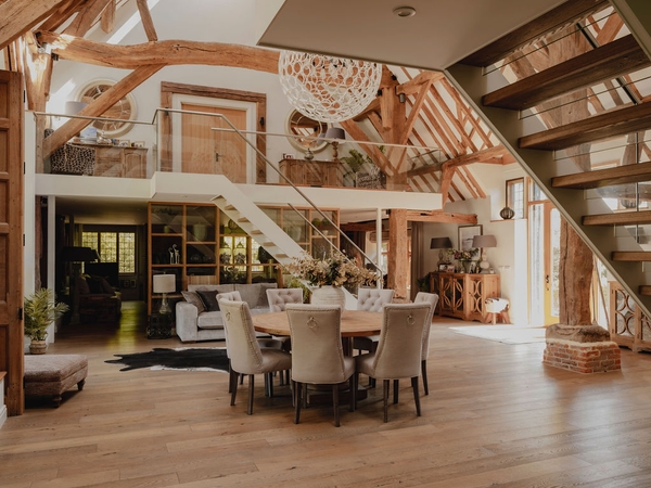 Overview of a vast barn conversion living space featuring high vaulted ceilings, statement lighting, and floating timber stairs, Love Locations RG9.