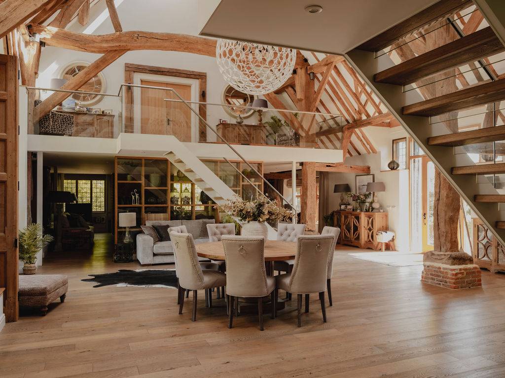 Overview of a vast barn conversion living space featuring high vaulted ceilings, statement lighting, and floating timber stairs, Love Locations RG9.