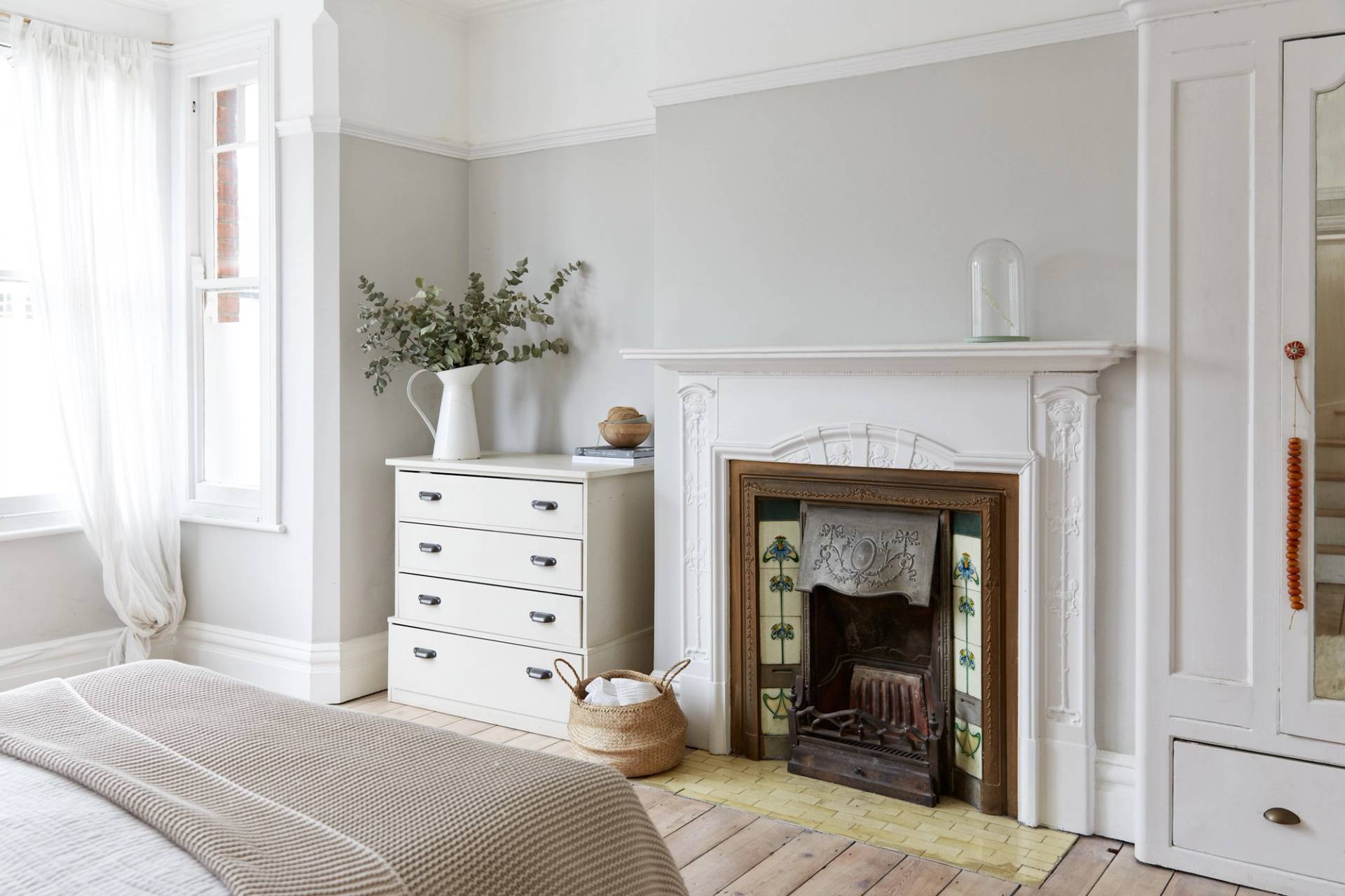 Period bedroom suite featuring a white painted fireplace mantel, floral tiled hearth surround, white chest of drawers, and stripped floors, Love Locations.