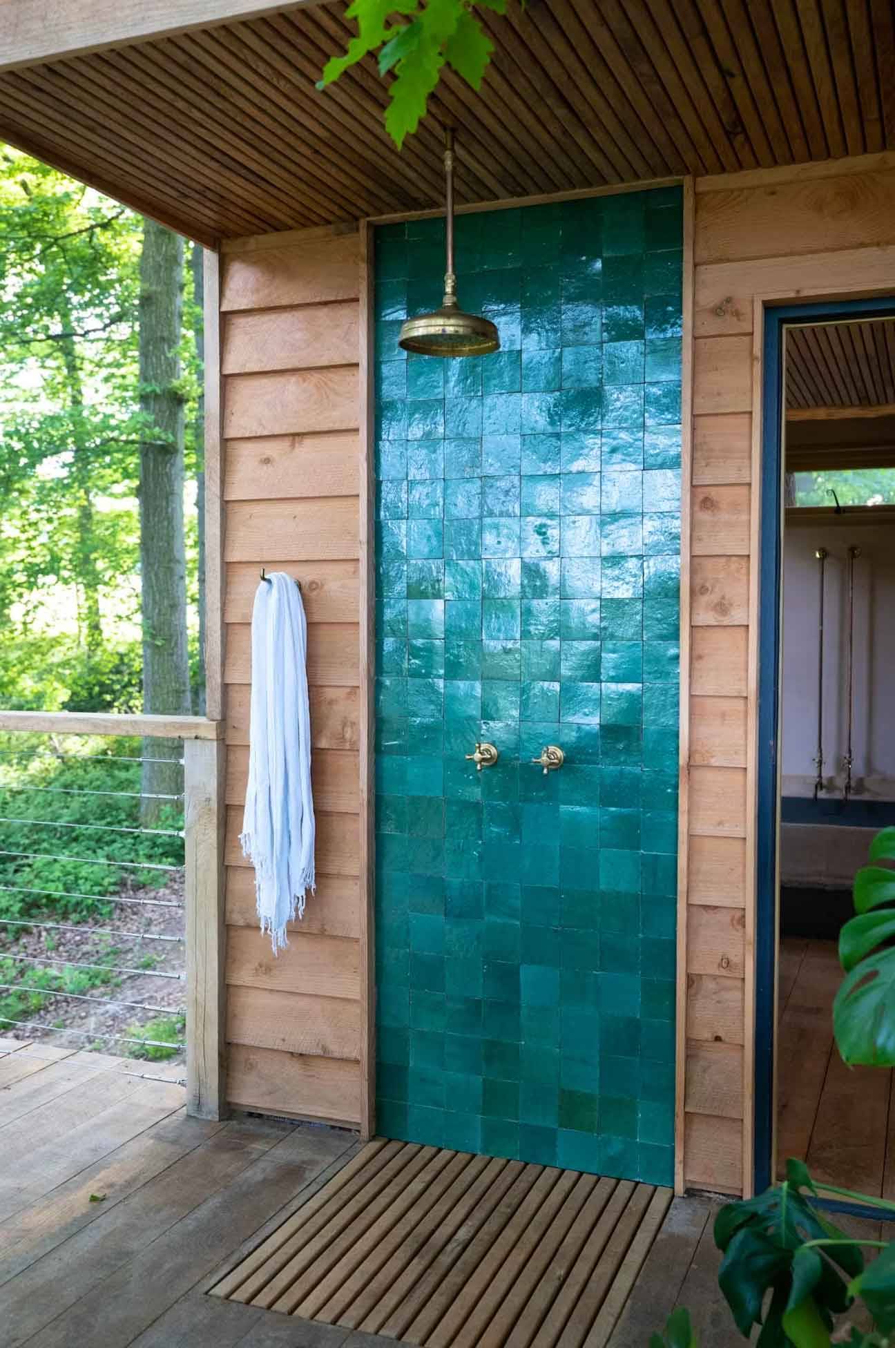 Luxury outdoor open-air shower clad in vibrant emerald teal green tiles on a natural wood cabin wall, managed by Love Locations HR4 8ls.