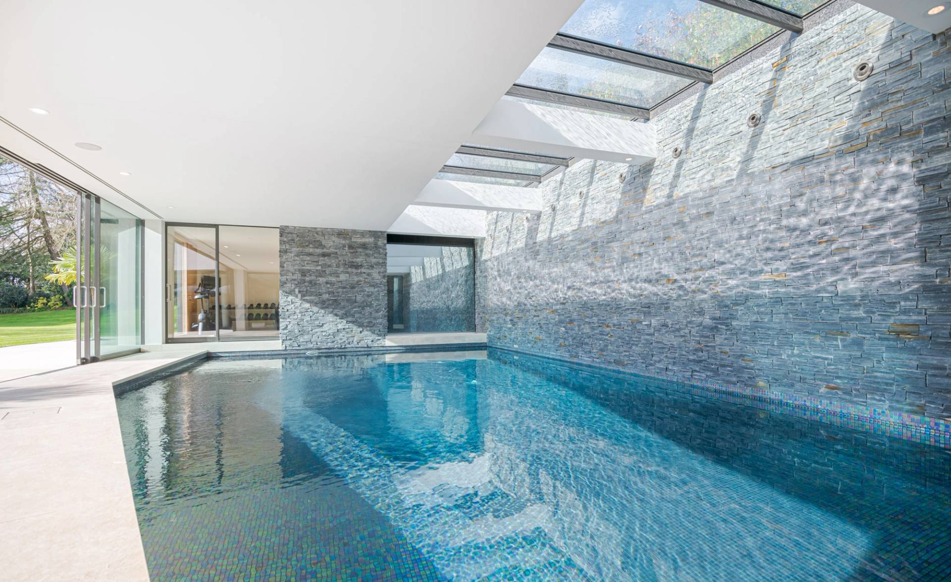 Symmetrical shot of a heated indoor swimming pool framed by grey slate stone walls and glass reflection doors, ideal for swimwear marketing, Love Locations KT2.