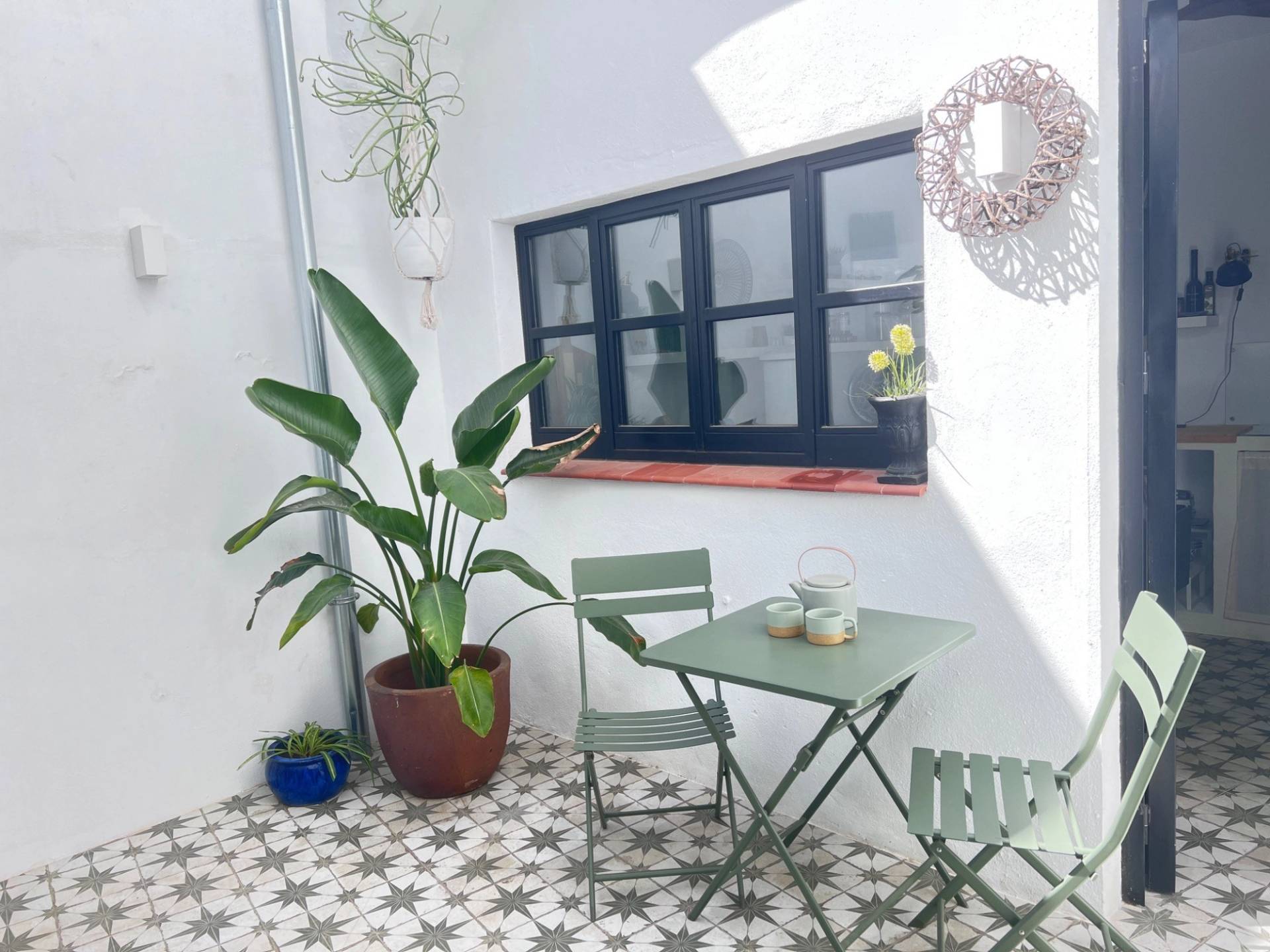 Charming Spanish courtyard garden photoshoot backdrop in Jimena de la Frontera by Love Locations, featuring a bistro table, green folding chairs, and potted greenery against white walls.