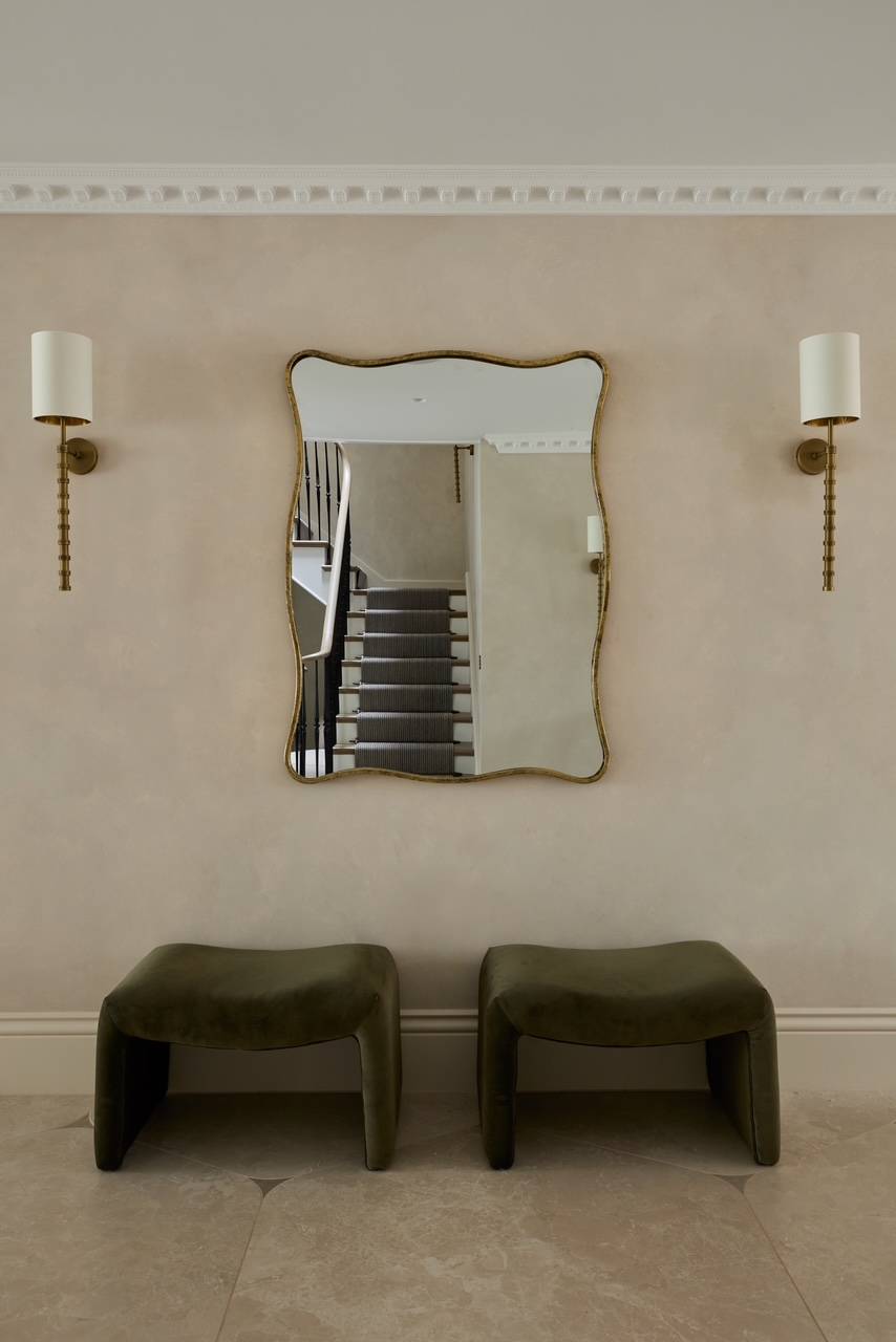 Elegant transitional hallway vignette showing twin olive green velvet stools beneath a decorative wavy gilt mirror, ideal for upscale home design lookbooks, Love Locations.