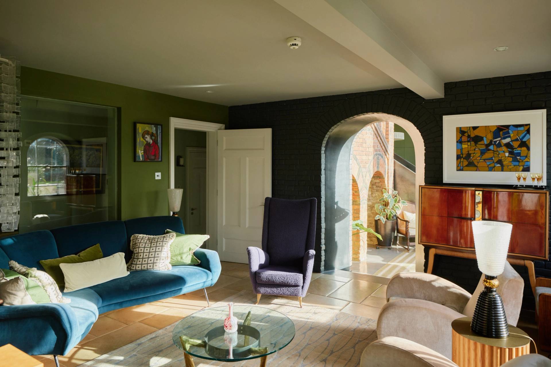 Spacious reception room with dark walls, navy velvet sofa, and exposed brick archways in Wimbledon, South West London, Love Locations.