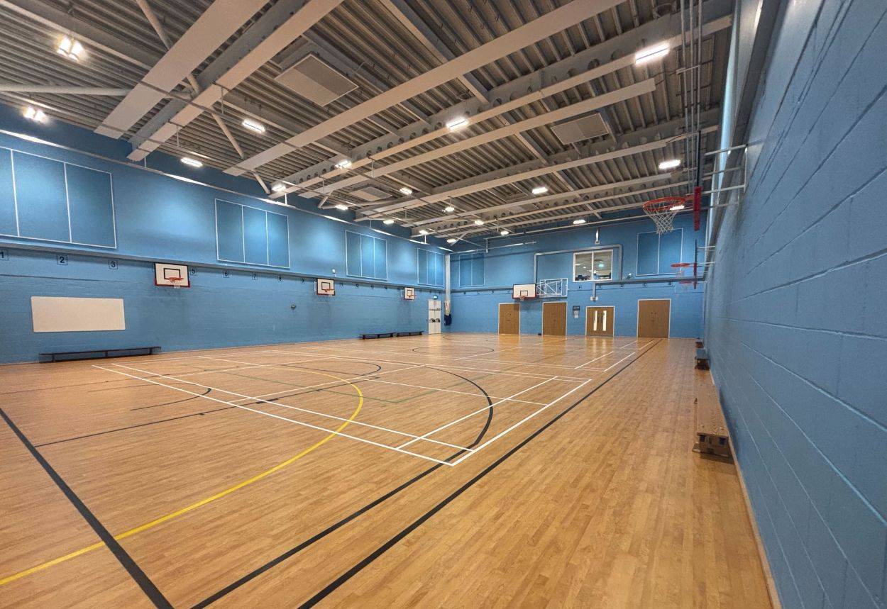 Large indoor sports hall film location in Sittingbourne Kent ME10, displaying blue walls, court line markings, and high ceiling rafters by Love Locations.