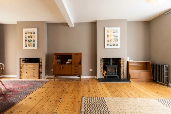 Love Locations period feature house East London E7: Cozy open-plan living room showing a cast iron log burner stove fireplace, vintage wooden credenza, and neutral tones, ideal for home branding campaigns.