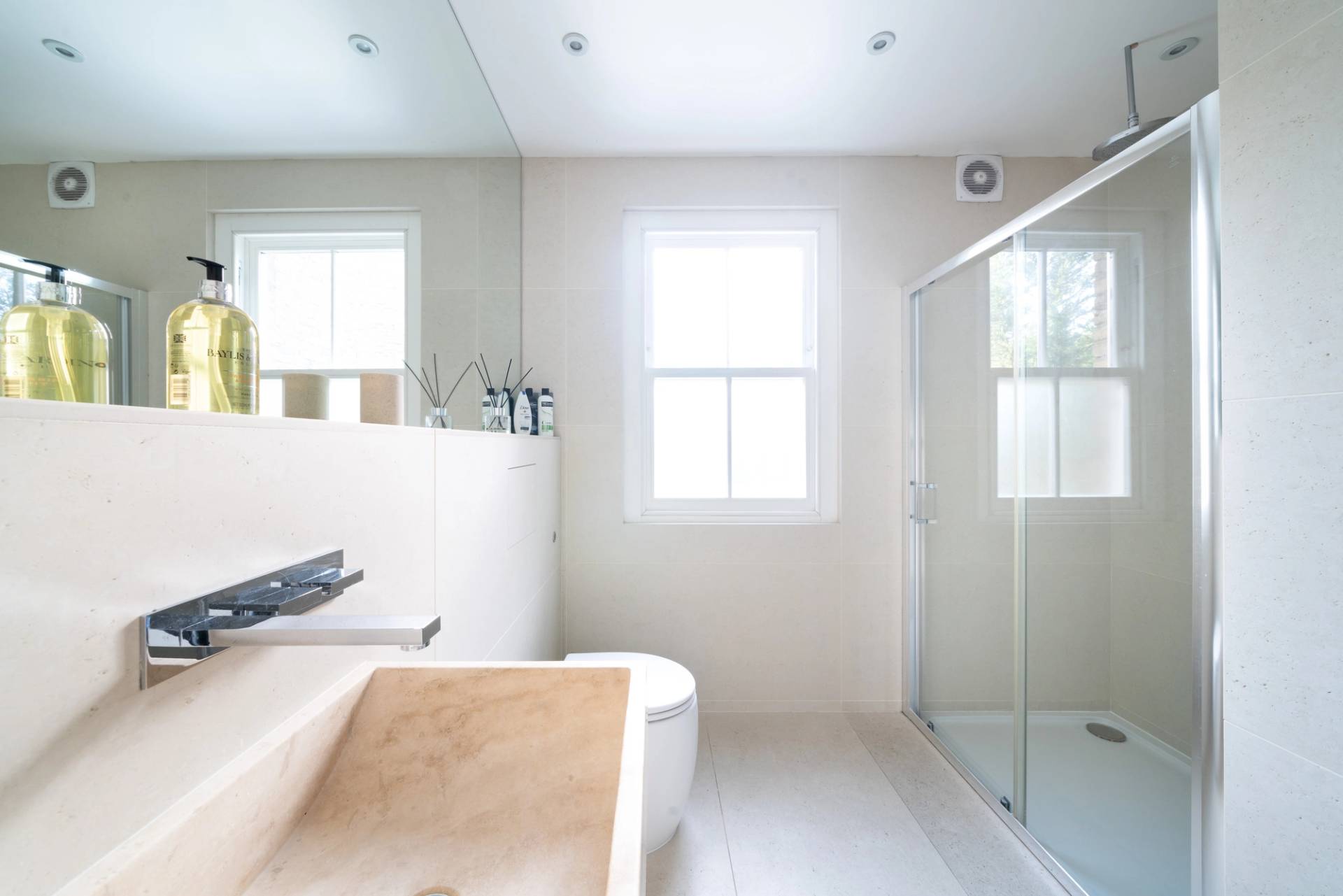 Modern bathroom with glass shower enclosure, beige wall tiles, and sash window views, Love Locations SW6.