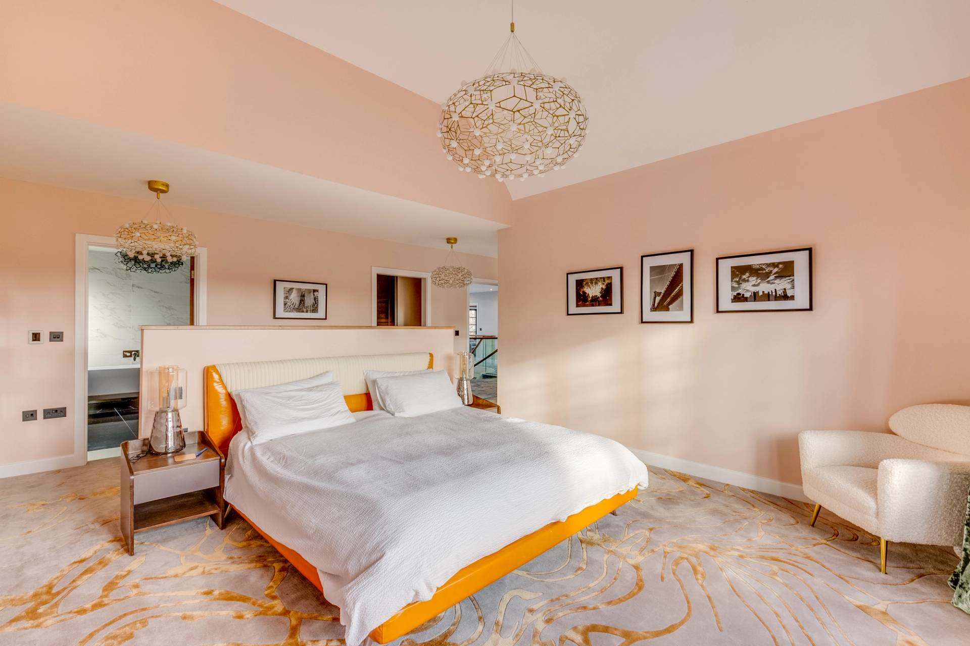 Master bedroom suite with pastel pink walls, upholstered white bed, and brass ring chandelier, Love Locations CB2.