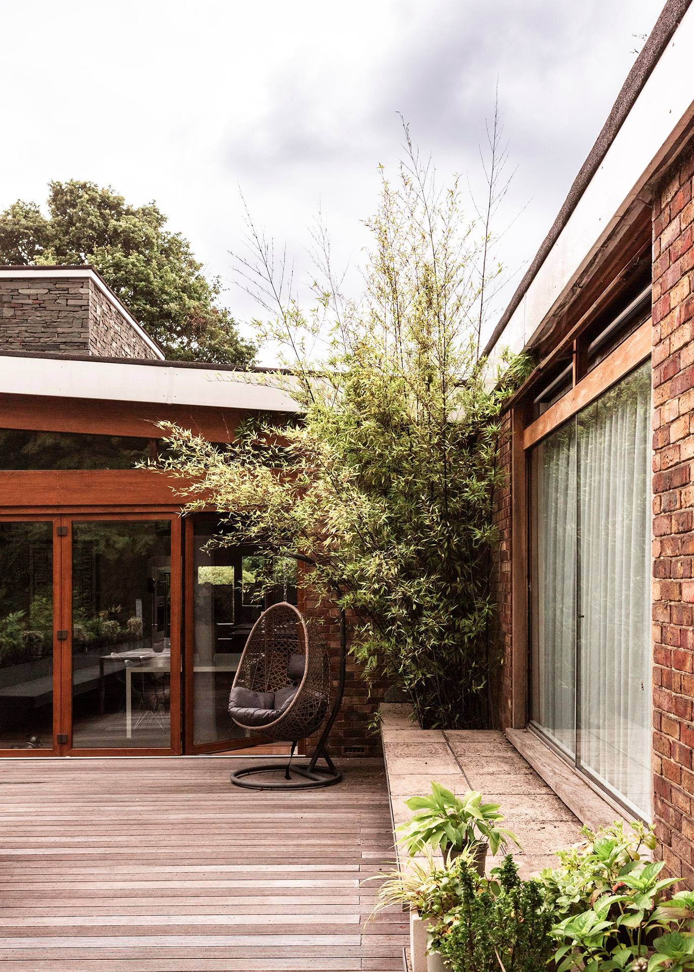 Sheltered outdoor seating nook on a timber deck featuring a hanging egg chair nestled against brick walls, Love Locations BR1.