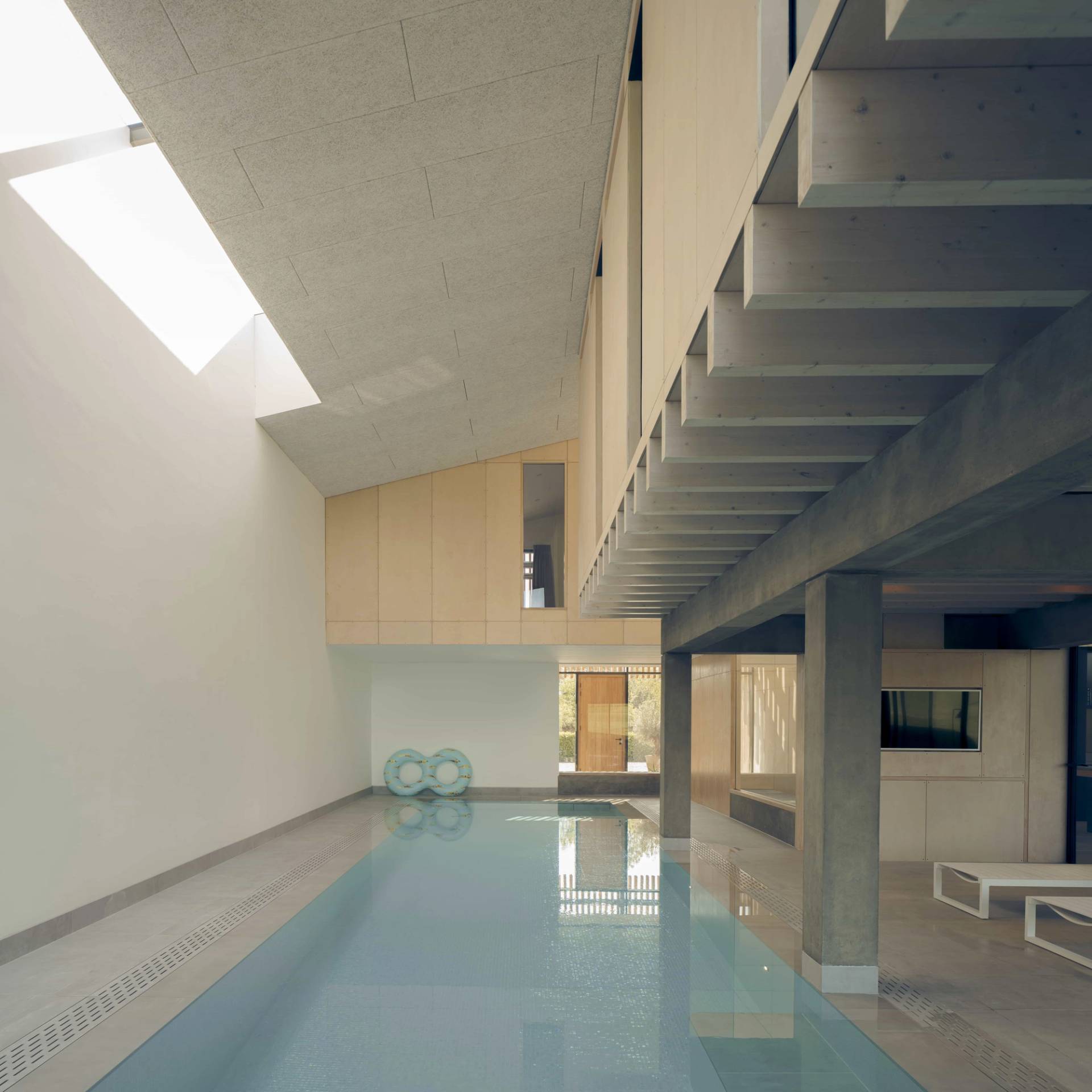 Minimalist indoor lap pool with sloped ceiling skylight, exposed concrete supports, and blue inflatable rings, Love Locations NR9.