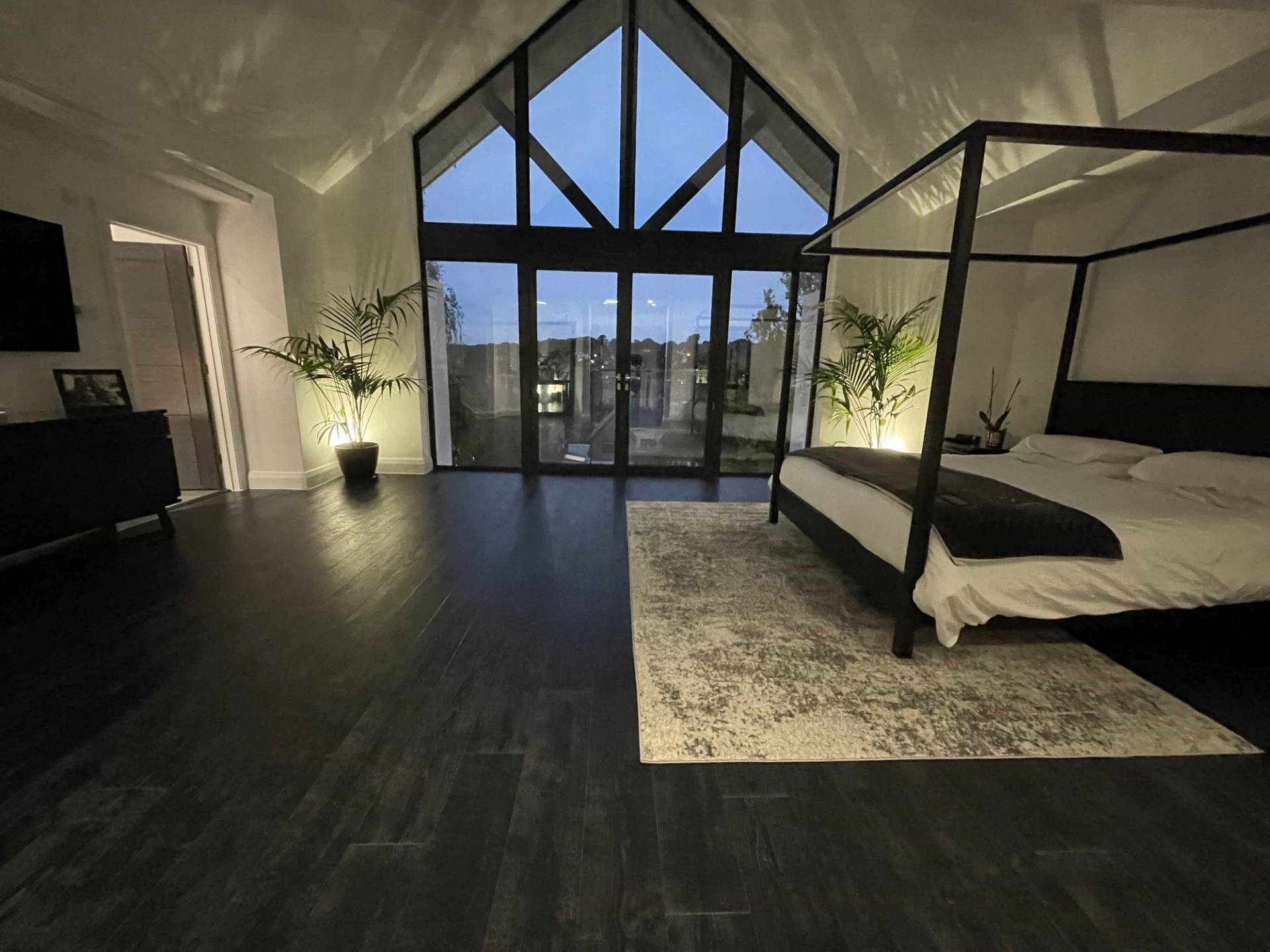 Vaulted master bedroom suite featuring a black four-poster bed set before full-height A-frame gable windows, Love Locations.