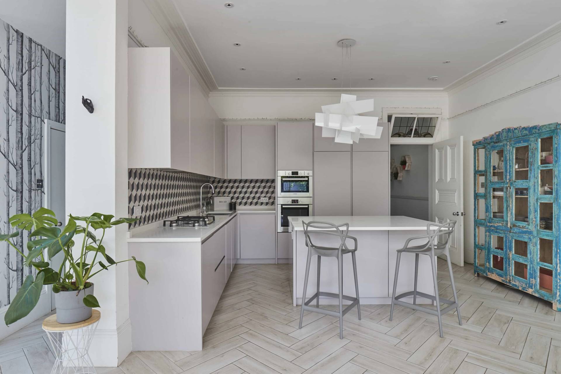 Sleek light grey kitchen island featuring white quartz countertops, geometric tile backsplash, and silver bar stools, Love Locations Ealing Common.