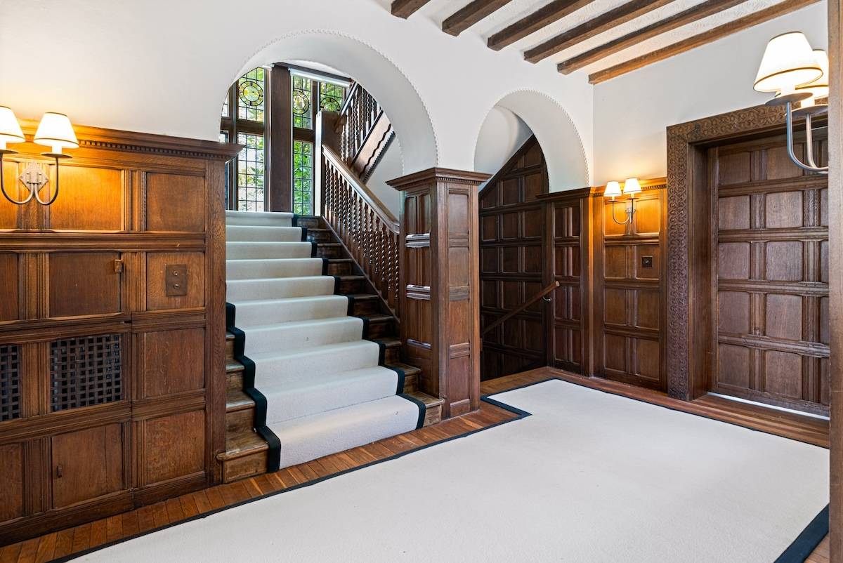 Grand wooden staircase balustrade set against rich oak wall panelling and white carpeted stairs, Love Locations RH13.