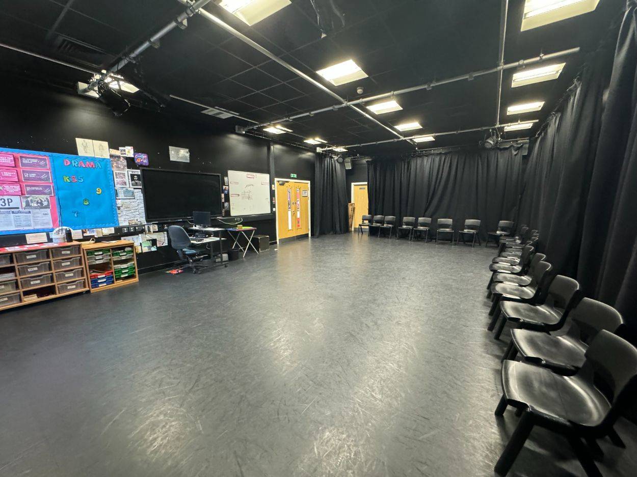 Black drama studio setup showing perimeter seating and stage props in a North Finchley school by Love Locations.