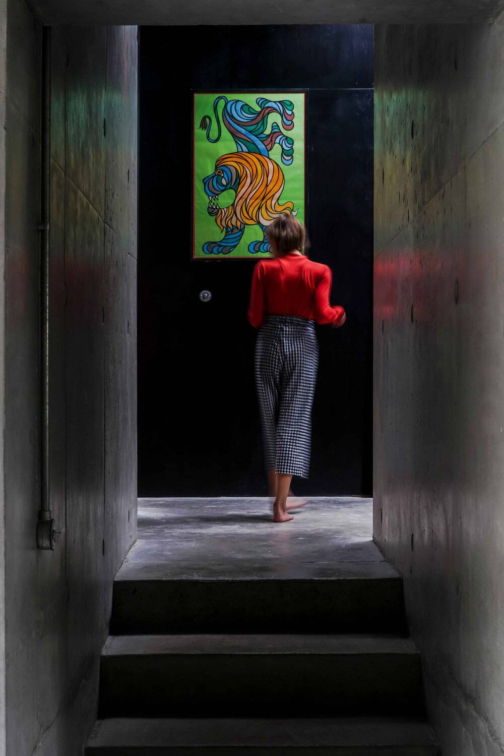 Raw concrete interior corridor looking towards a bright doorway with vibrant artwork and figure, Love Locations BN7.