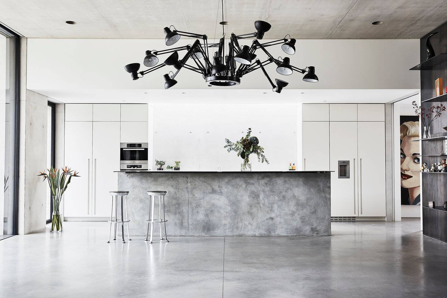 Minimalist luxury kitchen location with a polished grey concrete island, polished floorboards, crisp white cabinetry, and statement spider chandelier, perfect for high-end appliance advertising, Love Locations SW8.
