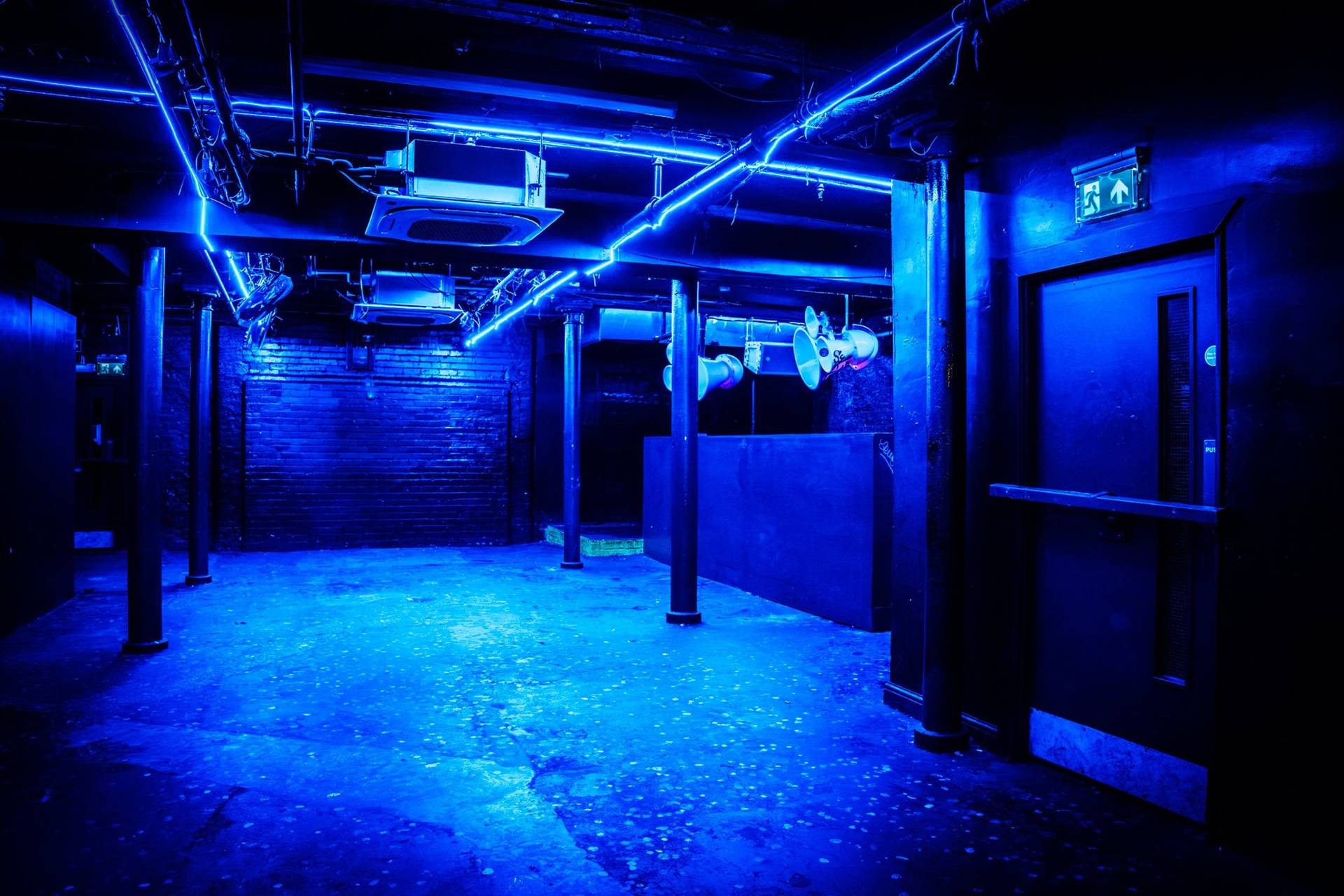 Electric blue lit event room featuring exposed ceiling pipes and industrial support pillars in a Manchester M3 venue via Love Locations.