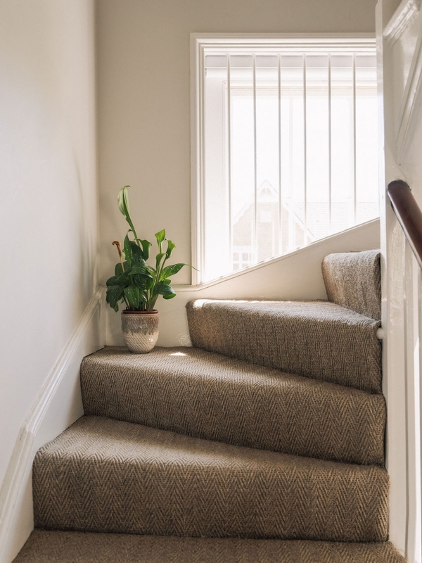 Upper floor staircase landing corner featuring a potted houseplant next to a bright window frame, Love Locations.