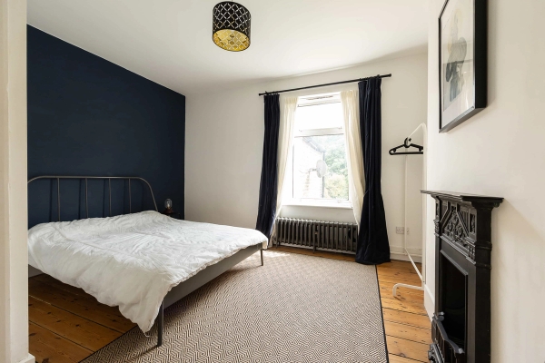 Love Locations atmospheric bedroom location E7: Modern guest bedroom featuring a rich dark blue feature wall, minimalist styling, and a clean geometric rug layout, tailored for TV drama productions.