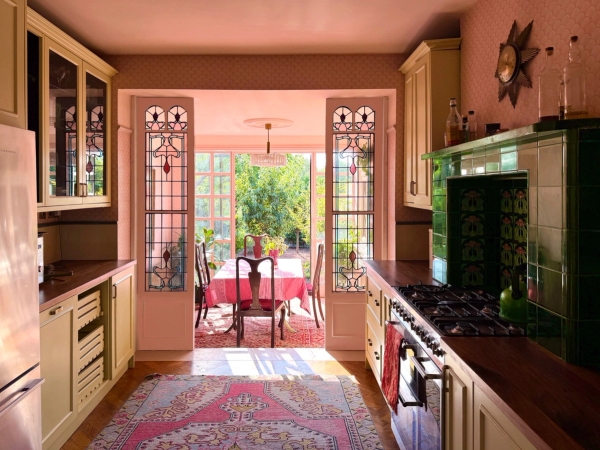Eclectic Edwardian kitchen with yellow cabinets, pink walls, and Art Nouveau stained glass doors leading to the garden in Palmers Green, Love Locations N13.