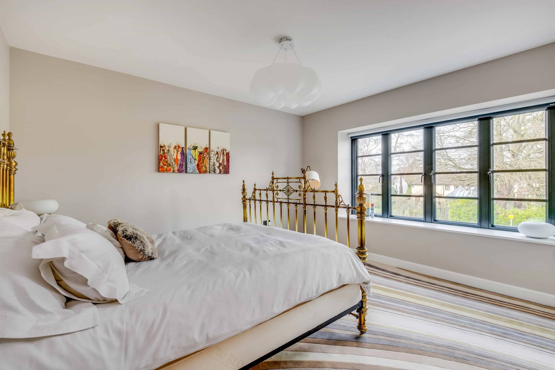 Guest bedroom featuring a vintage brass bed frame, white linen, and window light, Love Locations CB2.