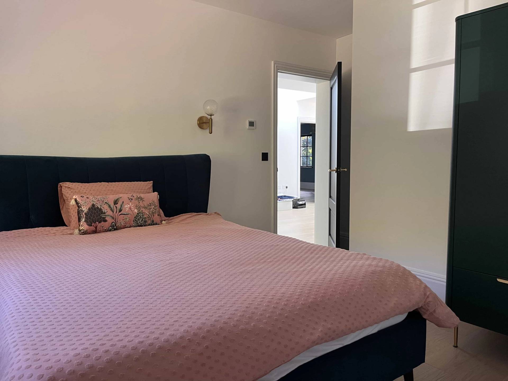 Minimalist master bedroom suite featuring a navy bed, pink bedspread, and en-suite doorway, Love Locations GU3.
