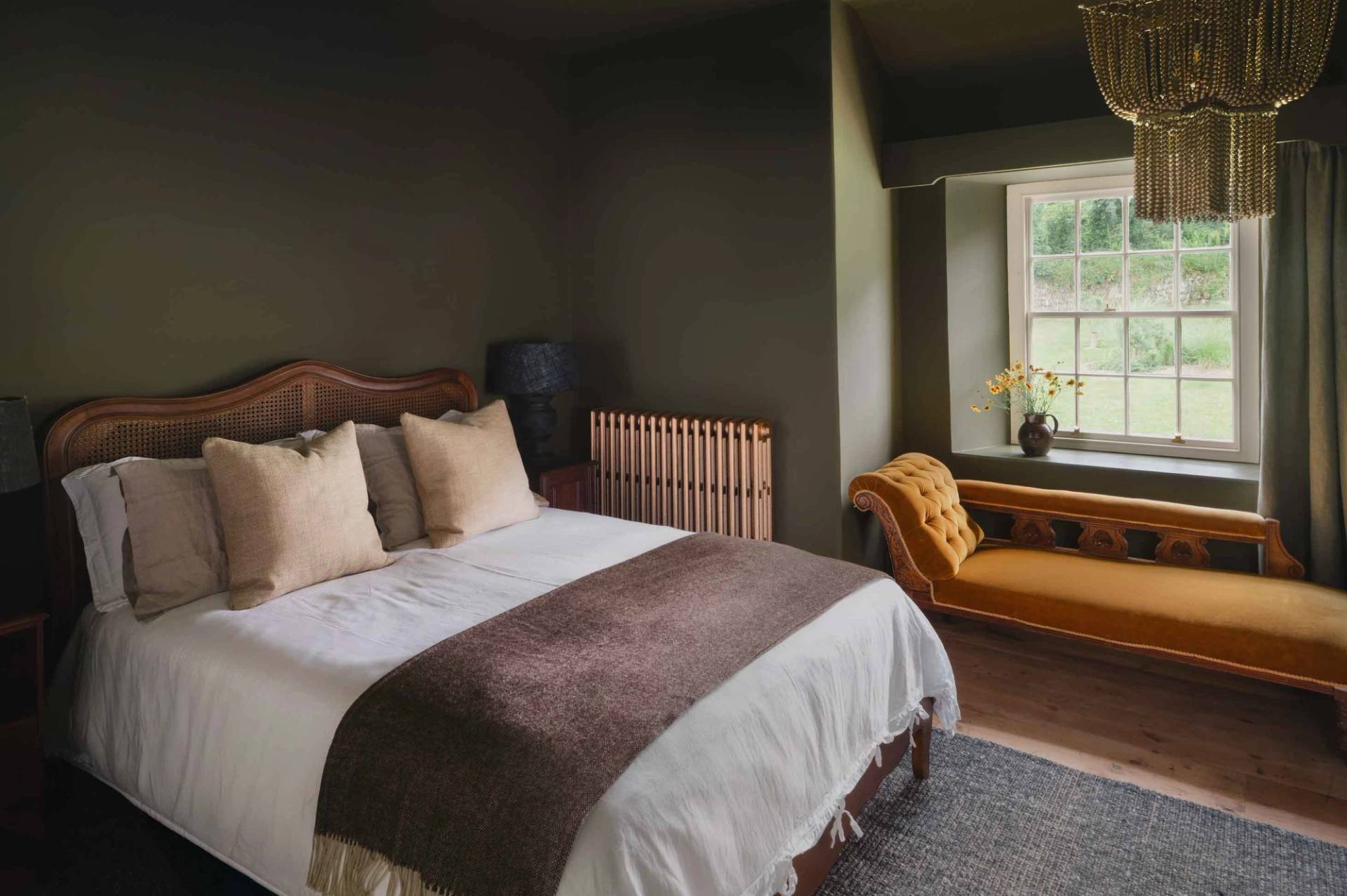 Olive green bedroom location house featuring a dark wood bed frame and mustard yellow velvet chaise lounge in Newquay from Love Locations.