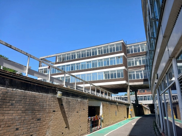 Retro industrial office building exterior for creative media production in Watford WD18 via Love Locations, highlighting a textured concrete retaining wall and elevated walkway.