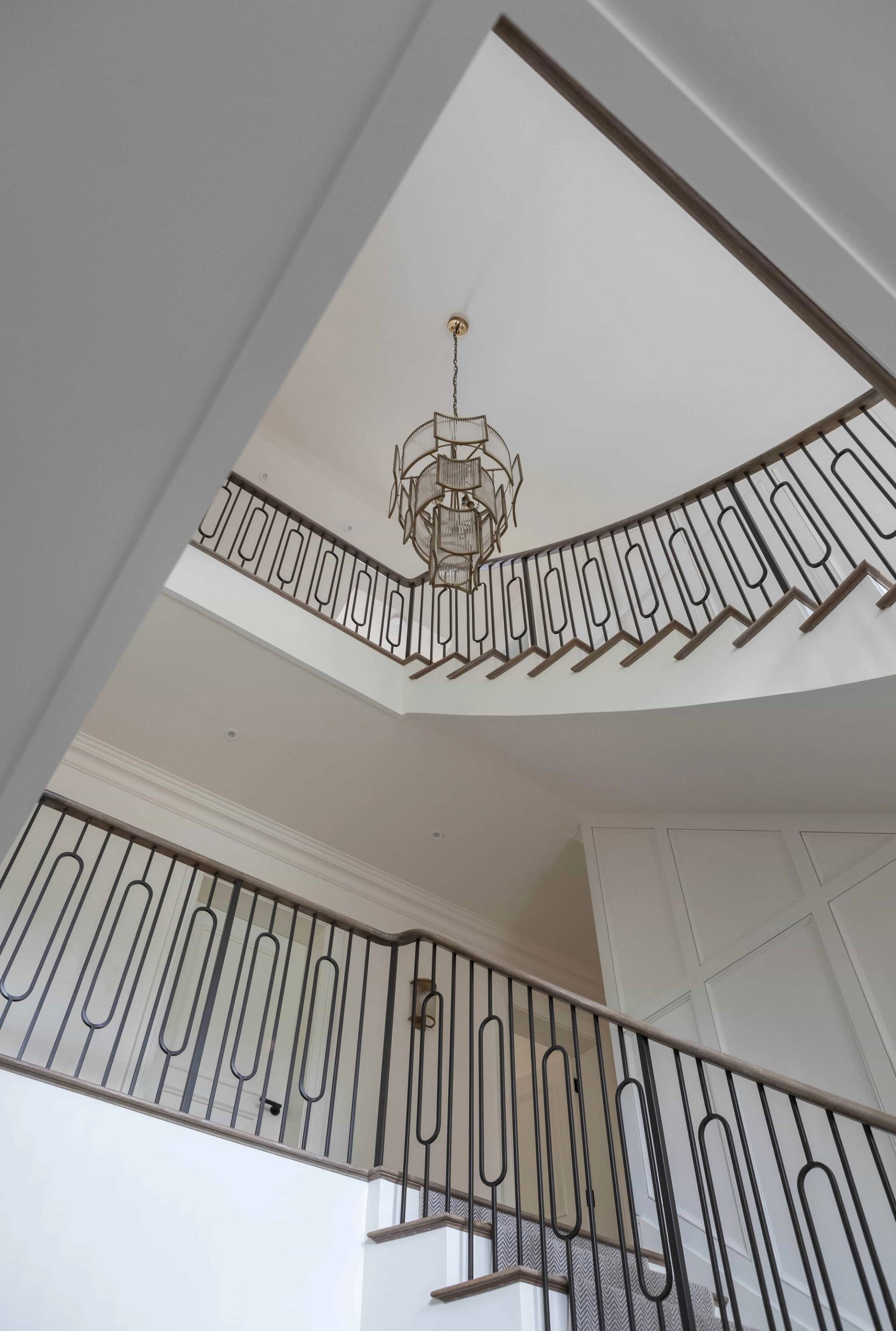 High-angle perspective of a grand curved staircase featuring intricate black iron balustrades and crystal chandelier, Love Locations HP18.