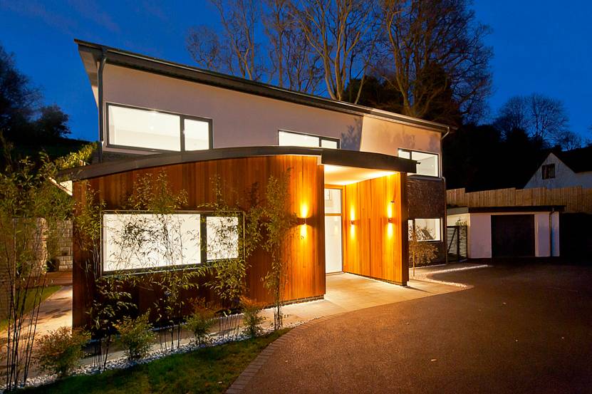 Stunning architectural front entrance facade illuminated at night with warm up-lighting on natural cedar cladding in Guildford, Surrey, GU5, the ultimate high-end backdrop for prestige automotive and luxury brand advertising via Love Locations.