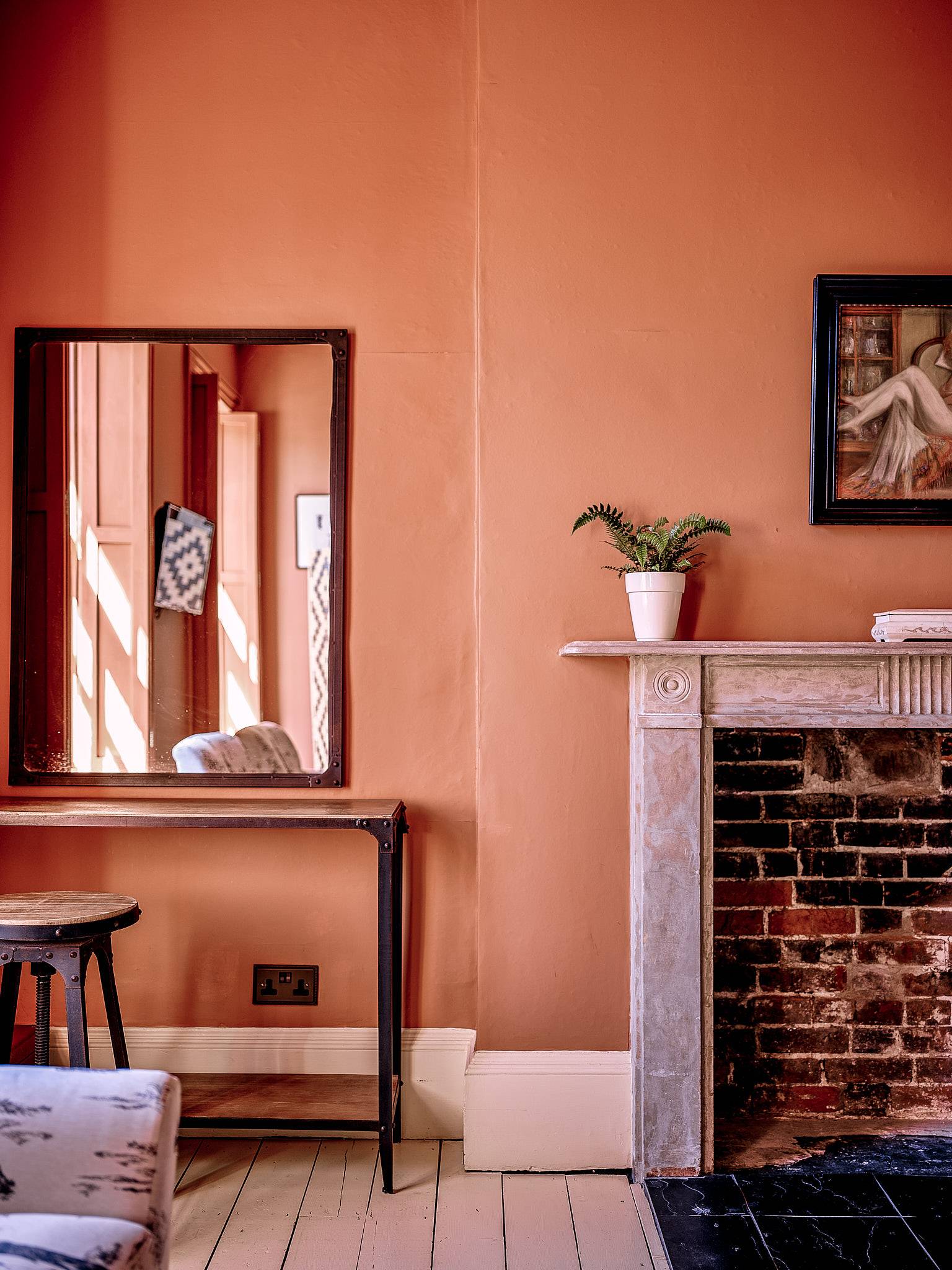 Terracotta pink bedroom wall with a wood-framed mirror and brick fireplace mantelpiece, Love Locations.