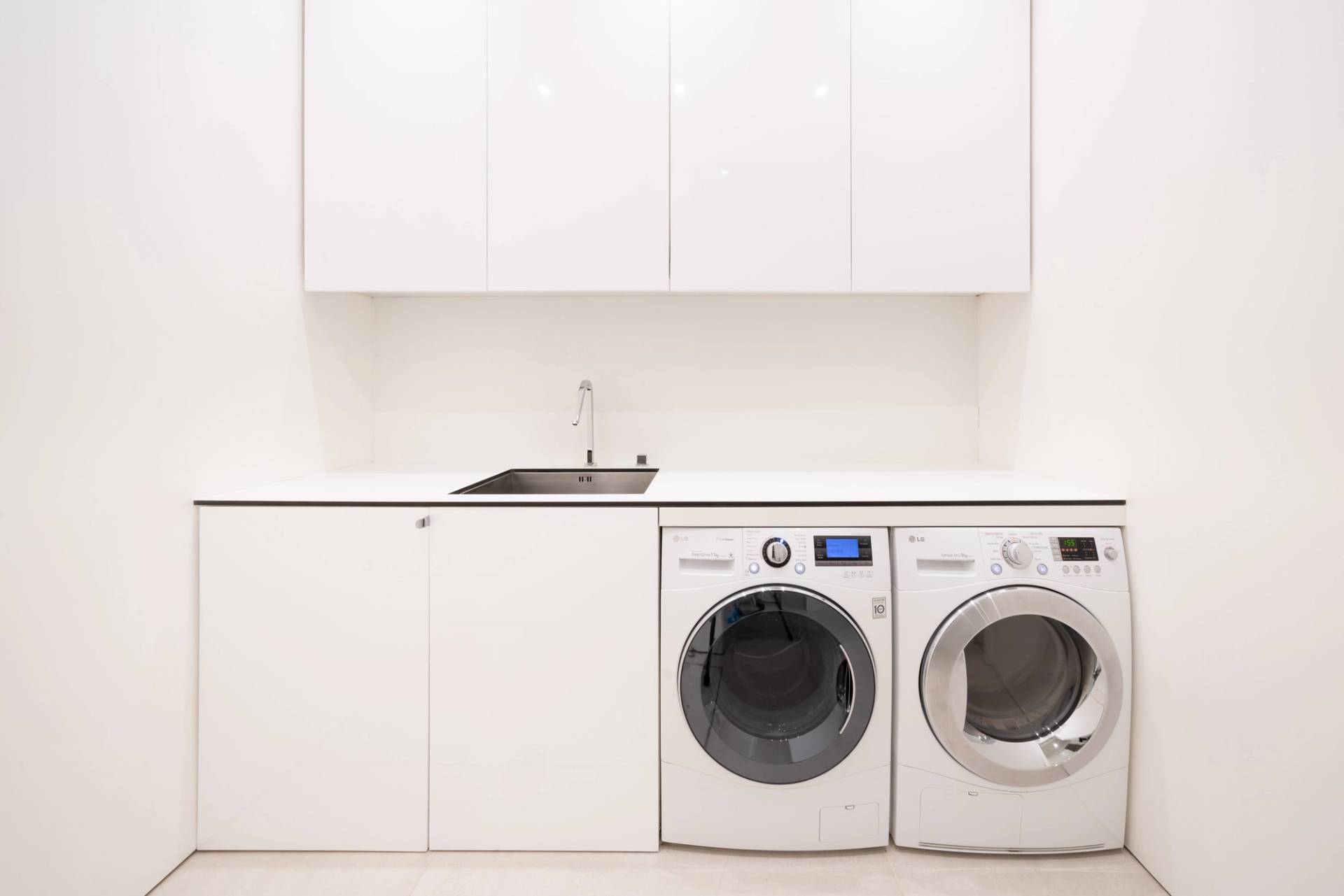 Minimalist white utility room featuring integrated LG washing machine, tumble dryer, sink, and overhead cabinets, Love Locations SW6.