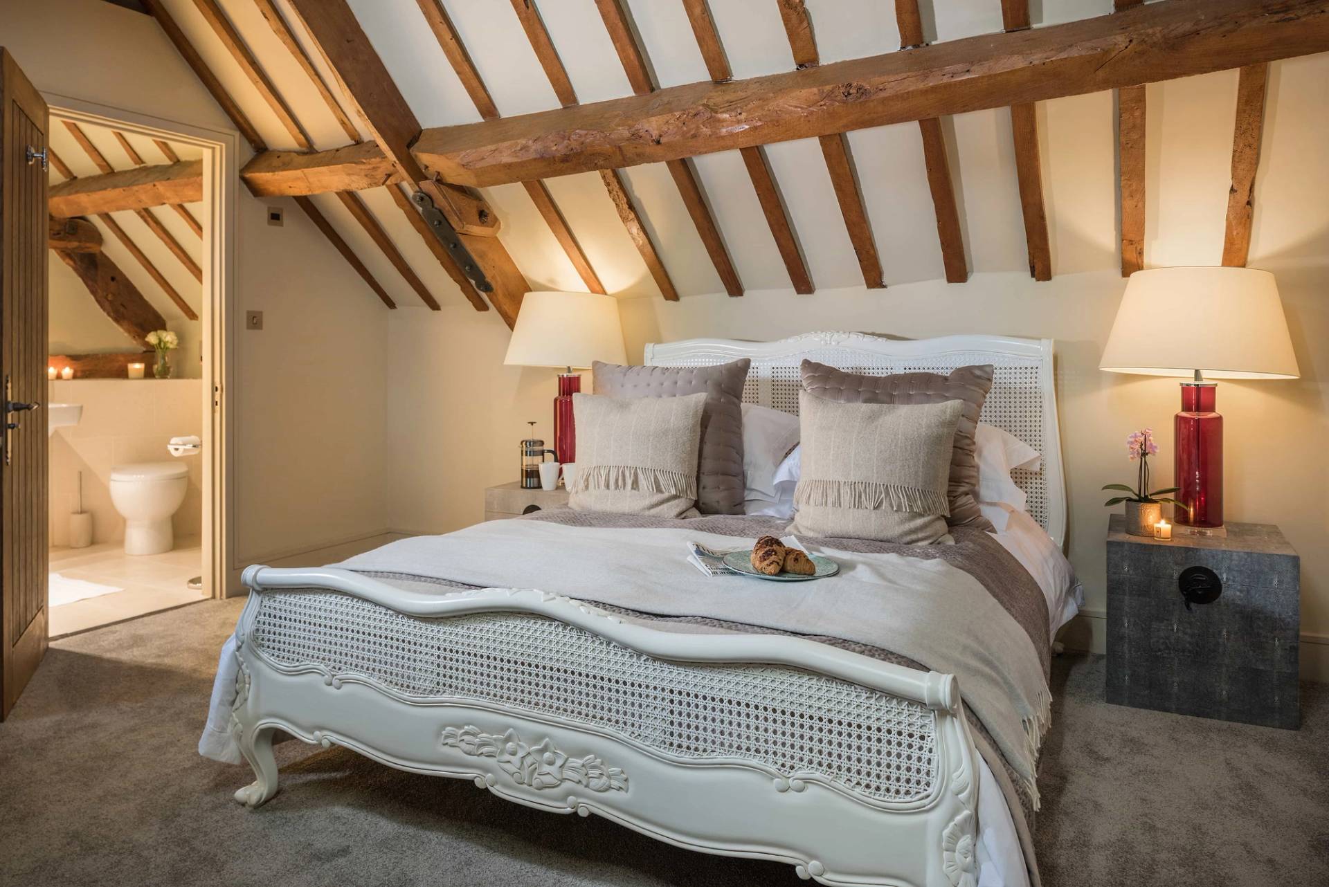 Characterful loft bedroom location in Cheltenham GL51 from Love Locations, displaying a white French country-style bed frame, exposed roof drapes, and warm natural lighting.